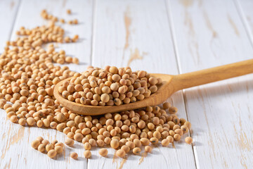 soybeans crumble from in a wooden spoon on a white wooden table.