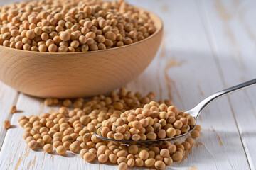 metal spoon with raw soybeans on a light table, selective focus.