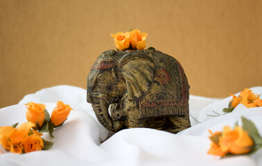 Antique Indian elephant statuette on white fabric and orange color flowers around. Space for copy...