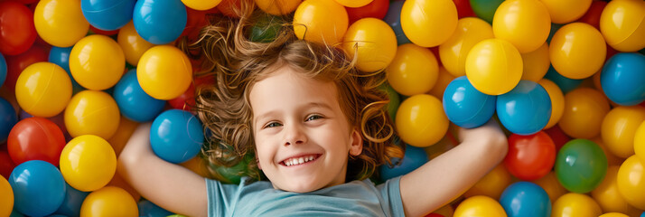 Fototapeta na wymiar Happy cheerful kid having a blast at indoor play center. Child playing with color balls in playground ball pit.