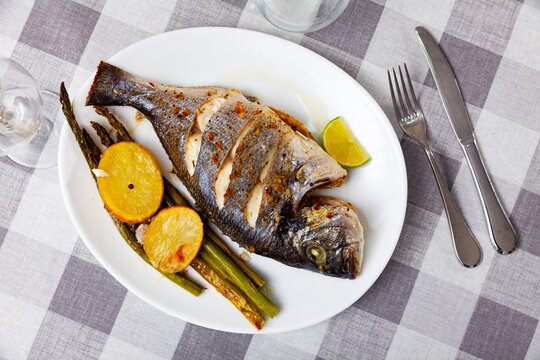 Appetizing baked dorada fish served with potatoes and asparagus on platter