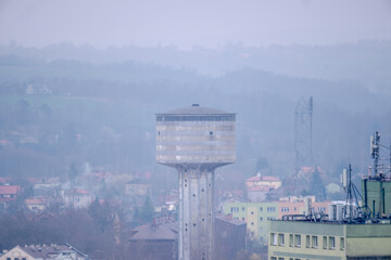 Stara charakterystyczna wieża ciśnień na terenie dawnej huty w Ostrowcu w mgliste marcowe popołudnie. Widok na miasto (jego historyczną część) w mglisty dzień o „świcie” wiosny. - obrazy, fototapety, plakaty