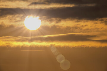 Zachodzące słońce na mocno zachmurzonym niebie. Słońce kolorowo zachodzące wśród chmur w ostatni dzień kalendarzowej zimy. - 768327861