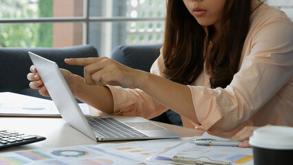 Asian Female freelance using laptop at home office desk. Woman reading financial graph chart...
