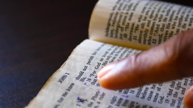 Hand pointing and gliding over John 3 verse 16 text on old bible page 2