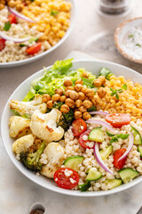 Vegan lunch bowl with roasted vegetables, fresh lettuce, cooked lentils, couscous salad and roasted chickpeas