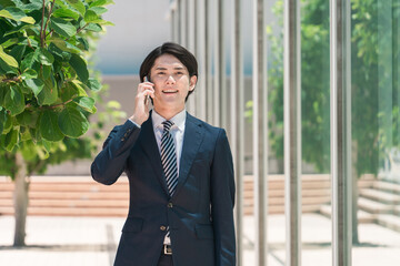 外回り中にスマホで通話するスーツ姿の若いアジア人男性ビジネスマン
