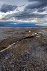 Small stream flowing through Death Valley at dusk with distant mountains and dramatic sky