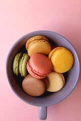 Purple cup filled with pastel macarons on pink background. Top view.