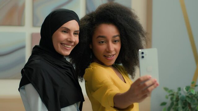 Diverse multiracial businesswomen happy joyful girls business partners Arabian muslim islamic in hijab and African American women posing together smile selfie photo on mobile phone camera in office