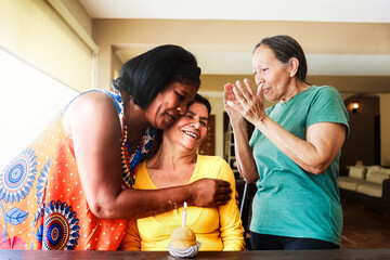 Multiracial senior friends celebrating birthday party together at home. Happy people hug each other. Elderly people, community concept