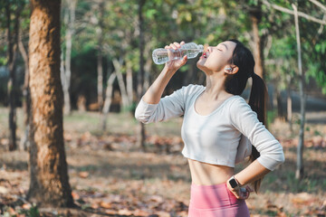 Young female athlete drinking water from a bottle after a workout, refreshing herself in a natural park setting.