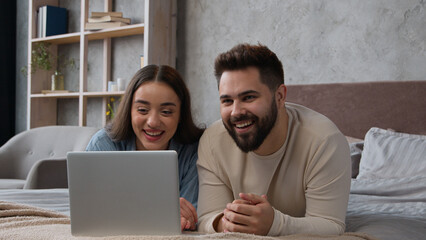 Caucasian family couple in love relaxing at home bedroom watch movie on laptop laughing talk online...
