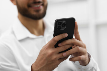Young man using smartphone indoors, selective focus