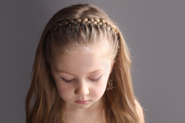 Little girl with braided hair on grey background. Space for text