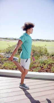 Vertical video: A biracial man is performing lunges outdoors on a wooden pathway