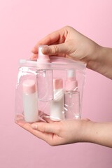 Cosmetic travel kit. Woman putting small bottle with personal care product into plastic bag against pink background, closeup