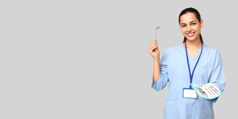 Portrait of female dentist holding dental tools on grey background with space for text