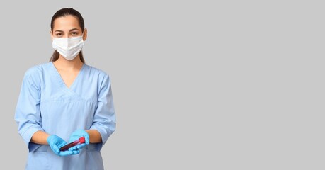 Portrait of female nurse holding test tube with blood sample on grey background with space for text