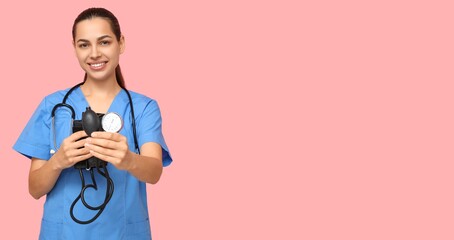 Portrait of female nurse holding sphygmomanometer on pink background with space for text