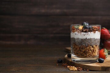 Tasty granola with berries, nuts, yogurt and chia seeds in glass on wooden table, space for text