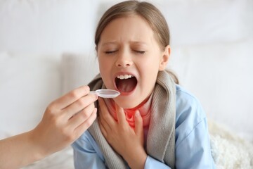 Ill little girl taking cough syrup at home