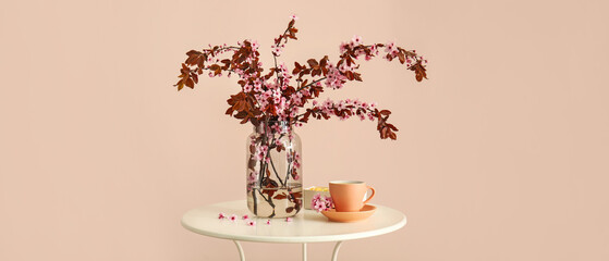 Vase with beautiful blossoming branches and cup of coffee on table against light background
