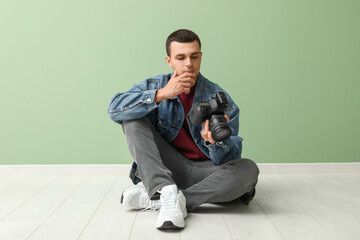Male photographer with modern camera sitting on floor in studio