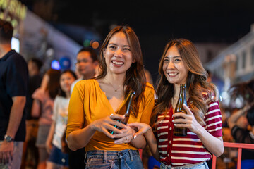Asian woman friends hold bottle of beer, having party in front of bar. 