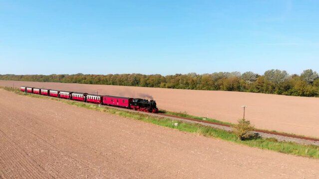 Aerial: steam narrow gauge railway in the countryside  passing by sown fields