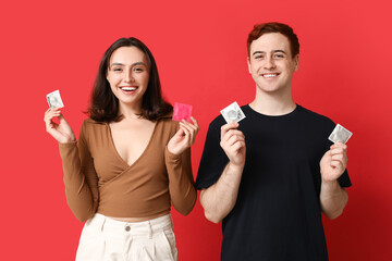 Young couple with condoms on red background. Safe sex concept - obrazy, fototapety, plakaty
