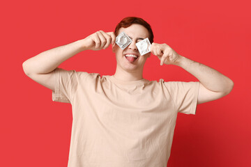 Funny young man with condoms on red background. Safe sex concept