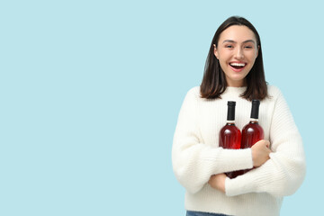 Beautiful young woman with bottles of red wine on blue background