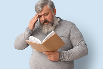 Portrait of sad senior man reading book on light blue background