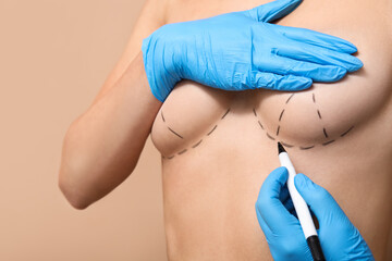 Doctor drawing marks on female breast before cosmetic surgery operation against brown background