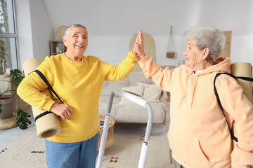 Senior female friends with fitness mats giving each other high-five at home