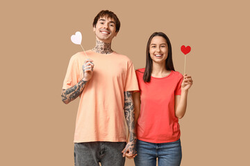 Young couple with paper hearts on beige background