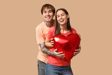 Young couple with heart-shaped air balloon on beige background