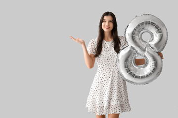 Beautiful young woman with silver air balloon in shape of figure 8 on grey background....