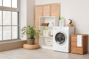 Modern washing machine with basket, shelving unit and dressing screen near white wall. Interior of...