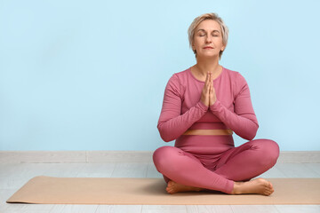 Portrait of meditating mature woman sitting on floor against blue wall