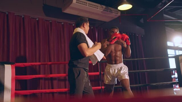 Asian fitness trainer support African sportsman doing boxing in gym. 