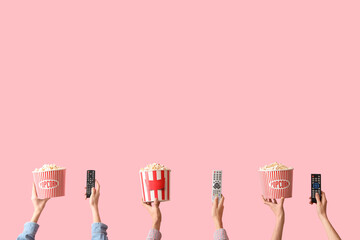 Hands with buckets of popcorn and TV remotes on pink background