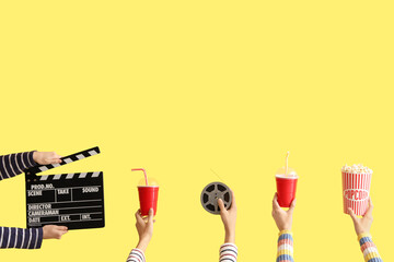 Many hands with movie clapper, bucket of popcorn and drinks on yellow background