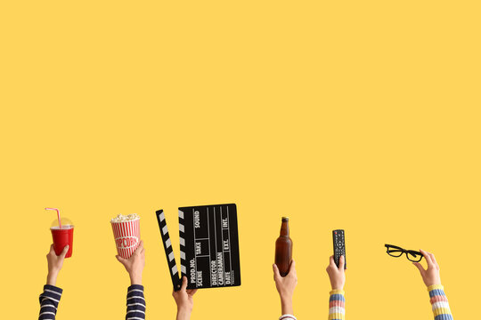 Many hands with movie clapper, bucket of popcorn and drinks on yellow background
