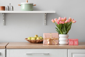 Calendar with date of International Women's Day, tulips and gift box on counter in kitchen
