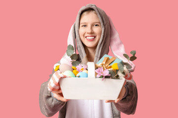 Obraz na płótnie Canvas Beautiful young happy woman in bunny costume with basket full of eggs on pink background. Easter celebration