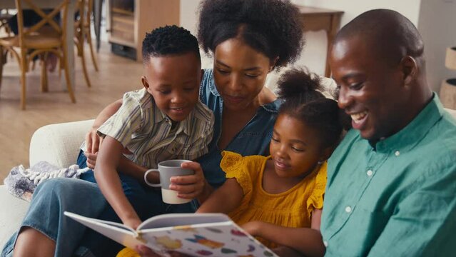 Family indoors at home sitting on sofa reading book together with grandparents in background - shot in slow motion