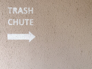 textured wall surface with stenciled trash chute sign with arrow