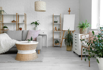 Loft style interior of comfortable living room with sofa, chest of drawers, table, houseplants, shelving units and easel - obrazy, fototapety, plakaty